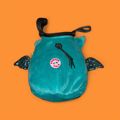 Teal coverted plush toy into handmade chalk bag with black glittery wings on an orange background back view of chalk bag with badge "Powder Pals"