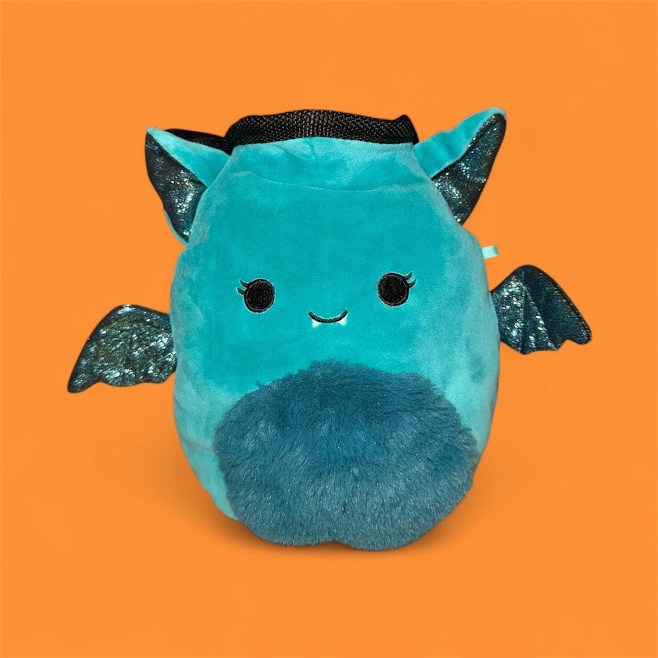 Teal coverted plush toy into handmade chalk bag with black glittery wings on an orange background front view