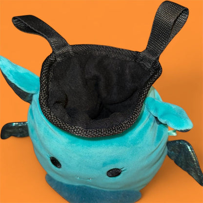 Teal coverted plush toy into handmade chalk bag with black glittery wings on an orange background top down view